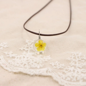 Détail d'un collier en résine fait main avec une véritable fleur séchée jaune