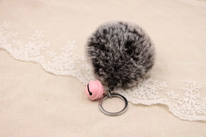 Detailed macro of fluffy grey and white faux fur keychain with pink bell on beige fabric