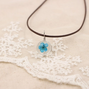 Gros plan d'un collier artisanal avec pétale de fleur séchée bleue en pendentif