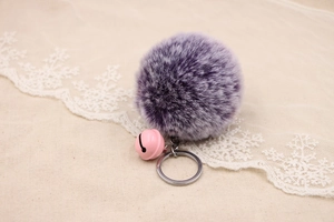 Close-up of a fluffy purple faux fur pompom keychain with a cute pink bell accessory