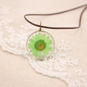 Vue macro d'une fleur séchée verte en résine transparente avec cordon tressé marron