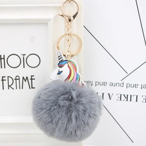 Close-up of fluffy grey pompom keychain with white unicorn and golden hardware