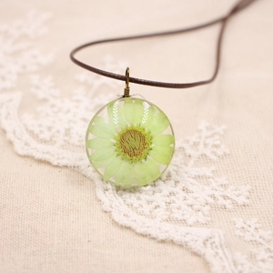 Macro d'un pendentif en boule de verre avec fleur séchée verte sur dentelle et lin