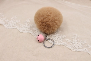 Close-up of khaki faux fur pompom keychain with pink bell and silver ring on lace fabric