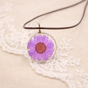 Macro d'une marguerite violette séchée scellée dans un pendentif rond en résine transparente