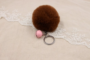 Detail of soft brown faux fur pompom keychain with a pink bell and silver ring