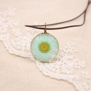 Gros plan d'un collier en résine avec marguerite bleue séchée et cadre en bronze