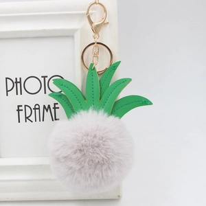 Detail of a pink pineapple faux fur pompom keychain with green leather leaves and gold hardware