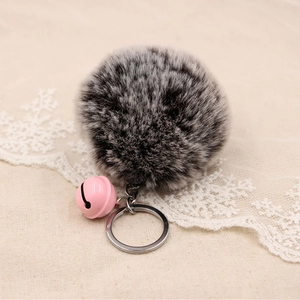 Close-up of soft faux fur pompom keychain with a pink bell on rustic burlap