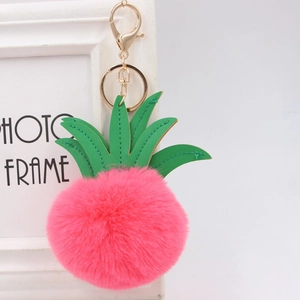 Close-up of pink fluffy pineapple pompom keychain with green faux leather leaf and gold clasp
