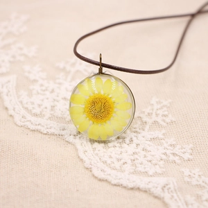 Vue rapprochée d'une marguerite jaune séchée dans un pendentif en verre avec cordon brun