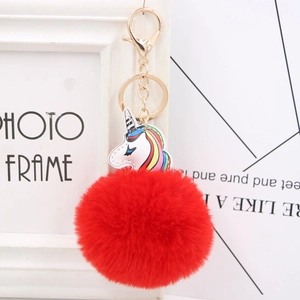Detail of colorful unicorn charm with large red faux fur pompom and golden metal keychain