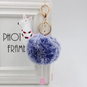 Dettaglio portachiavi con pompon viola, ciondolo alpaca e gancio in metallo dorato