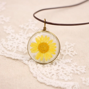 Collier artisanal en résine avec marguerite séchée et fil doré sur cordon brun