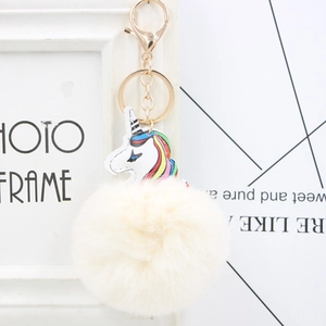 Detail of a white faux fur pompom keychain featuring a colorful unicorn with golden metal clasp