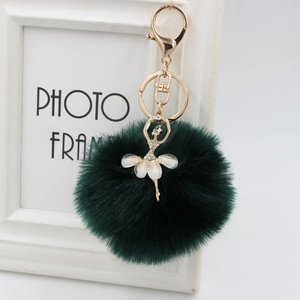 Close-up of elegant gold ballerina charm with rhinestones on dark green plush pom-pom