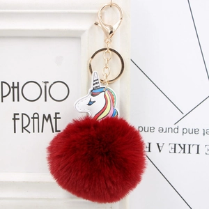Detail of colorful plush unicorn keychain with dark red faux fur pompom and golden ring