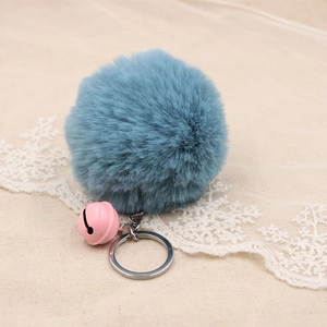 Close-up of soft blue faux fur pompom keychain with a pink bell on rustic linen fabric