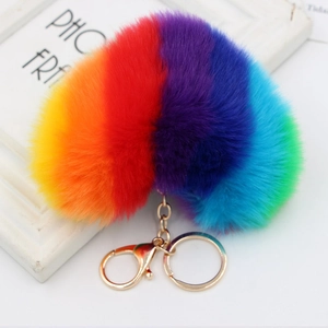 Detail of a fluffy rainbow heart pompom keychain with a gold lobster clasp on white frame
