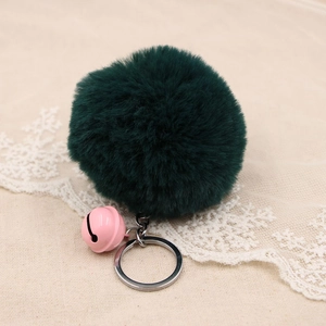 Detail of dark green faux fur pompom with pink bell and silver metal keychain ring