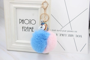 Detail of pink and blue fluffy pom pom keychain with a golden unicorn leather charm