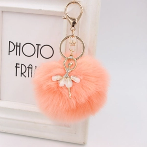 Detail of peach plush ball keychain with golden ballerina figurine and shiny lobster clasp