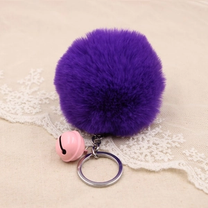 Macro view of dark purple faux fur pompom keychain with pink bell on beige fabric