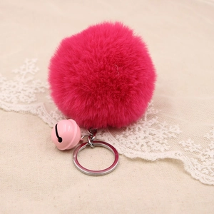 Detail of soft faux rabbit fur pompom keychain in rose red with a pink bell charm