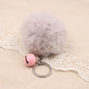 Close-up of soft grey plush ball keychain with pink bell on beige linen background