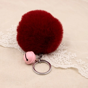Detail of burgundy faux fur pompom keychain with pink bell on beige lace background