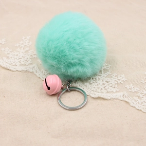 Mint green plush pompom keychain with pink bell and silver ring on lace fabric