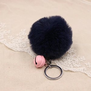 Close-up of fluffy dark blue pom pom keychain with a pink bell on textured fabric