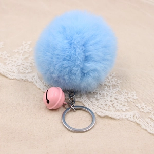 Detail of light blue faux fur pompom keychain with a pink bell and silver metal ring