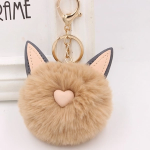Détail d'un porte-clés pompon en peluche kaki avec oreilles et coeur rose mignon