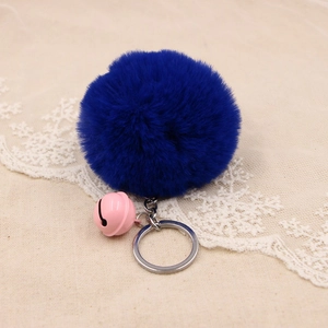 Deep blue faux fur pompom keychain with a light pink bell on beige woven fabric