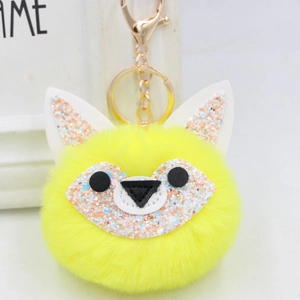 Close-up of bright yellow fluffy fox pompom keychain with golden metal ring and lobster clasp