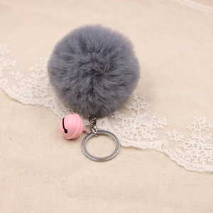 Macro shot of fluffy grey faux fur pompom with pink bell and silver keychain ring