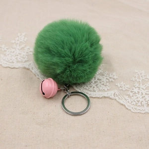 Detail of emerald green faux fur pompom keychain with a small pink bell and silver ring