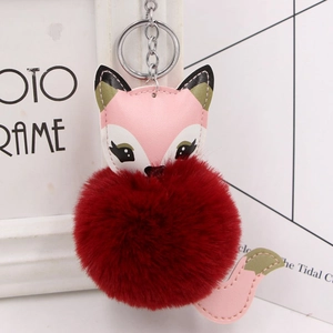 Close-up of cute fox pompom keychain in pink and burgundy faux fur for bag decoration