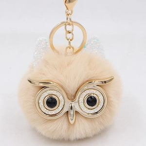 Detail of cute owl plush keychain with large glitter eyes and fluffy beige faux fur texture