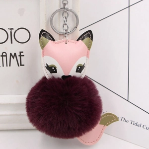 Detail of cute fox plush keychain with fluffy burgundy pom pom and pink leather trim