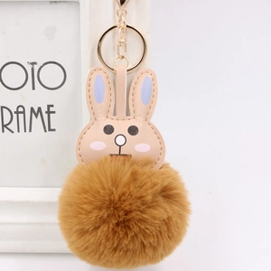 Cute brown rabbit plush pom pom keychain with gold ring hanging on a white frame