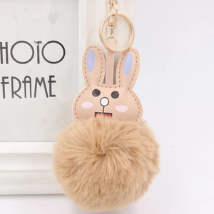 Close-up of cute rabbit faux fur keychain with light brown plush ball and golden ring clip