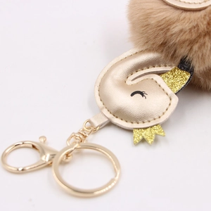 Detailed close-up of golden PU leather swan keychain with brown fur ball and lobster clasp
