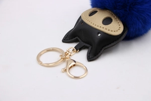 Close-up of navy blue plush keychain with gold metal clasp and leather eye details