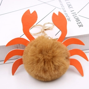 Détail d'un porte-clés crabe en peluche avec pompon marron et pinces en cuir orange vif