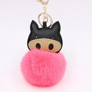 Close-up of pink fluffy pompom keychain with black faux leather pig head and golden clasp