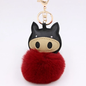 Detail of cartoon pig plush keychain with red faux fur ball and gold metal clasp