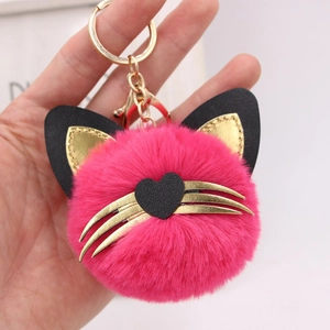 Detailed close-up of a pink plush cat keychain with golden whiskers and heart face charm