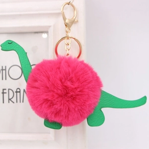 Detailed close-up of a green faux leather dinosaur charm with a fluffy magenta pom pom
